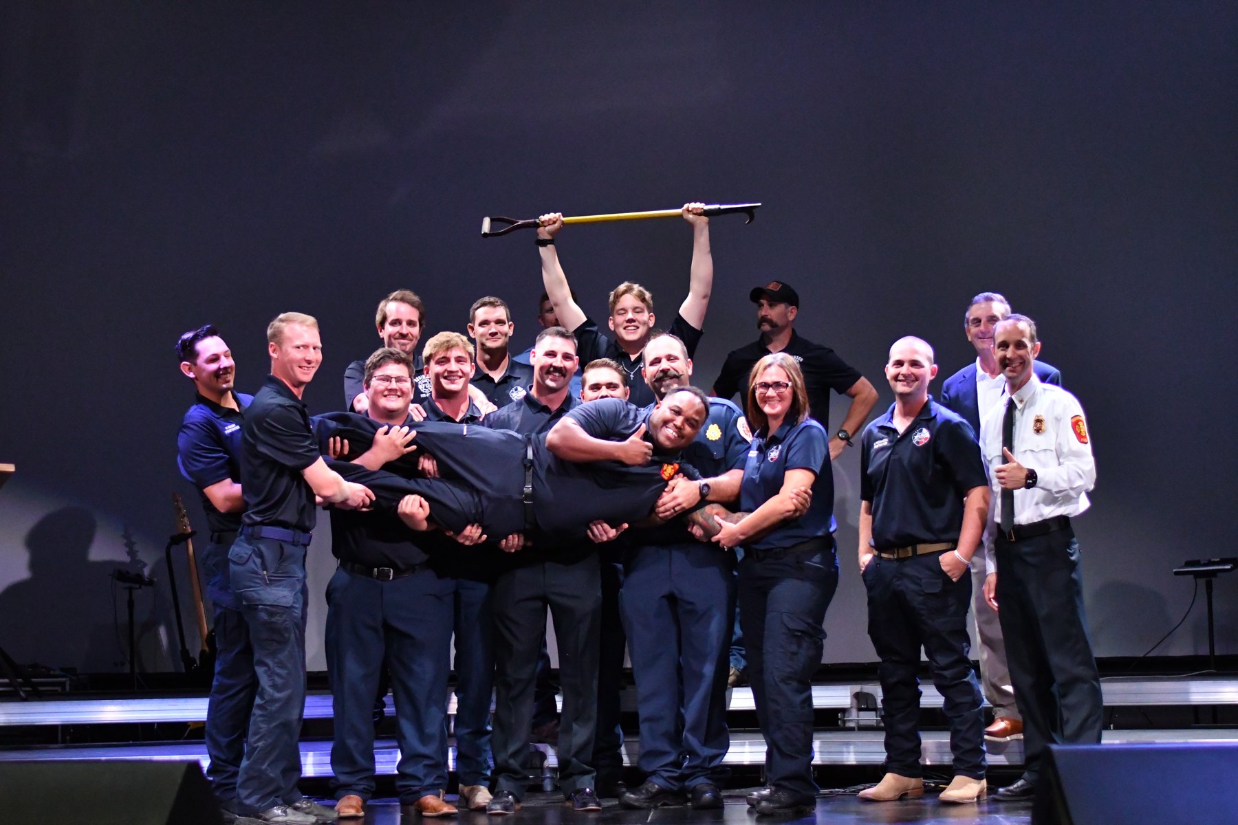 The Elm Mott crew celebrates together on stage after a graduation, lifting a member overhead